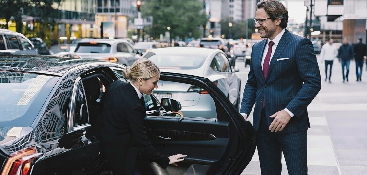Chauffeur in Frankfurt öffnet einem Geschäftsmann im Anzug die Tür einer schwarzen Limousine in der Innenstadt